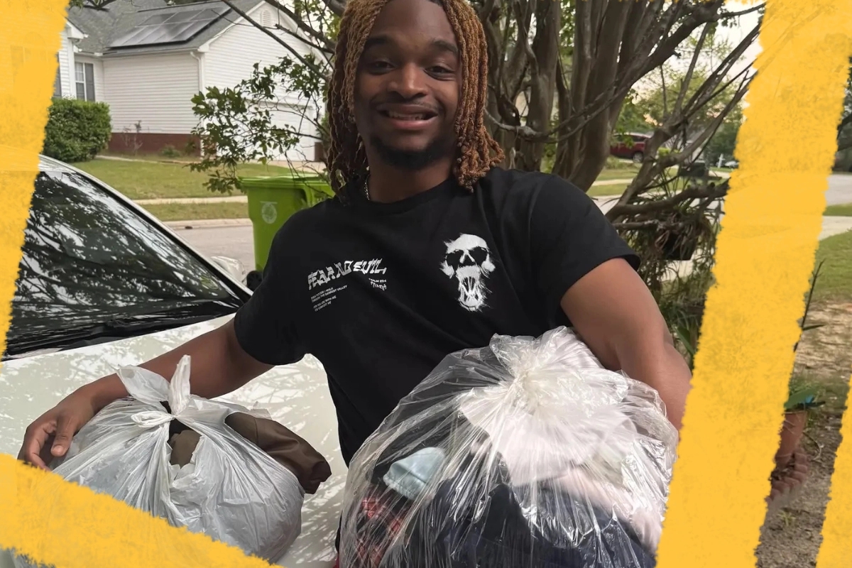 A smiling individual stands outdoors, holding two bags of collected items for donation. This image highlights community service and volunteer efforts in supporting local initiatives.